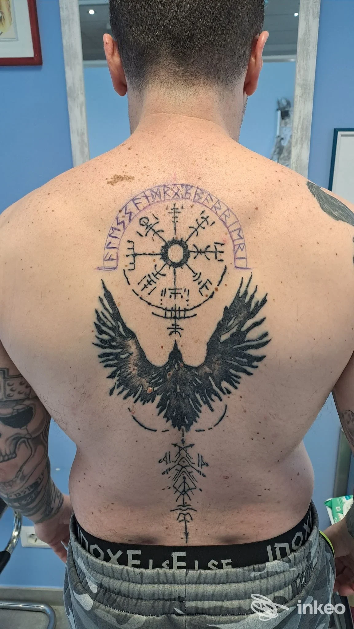 Tatuaggi neri sul dorso di un cliente nello studio Nuvola Rossa Tattoo a Castelletto sopra Ticino, motivo circolare e figura alata lungo la colonna.