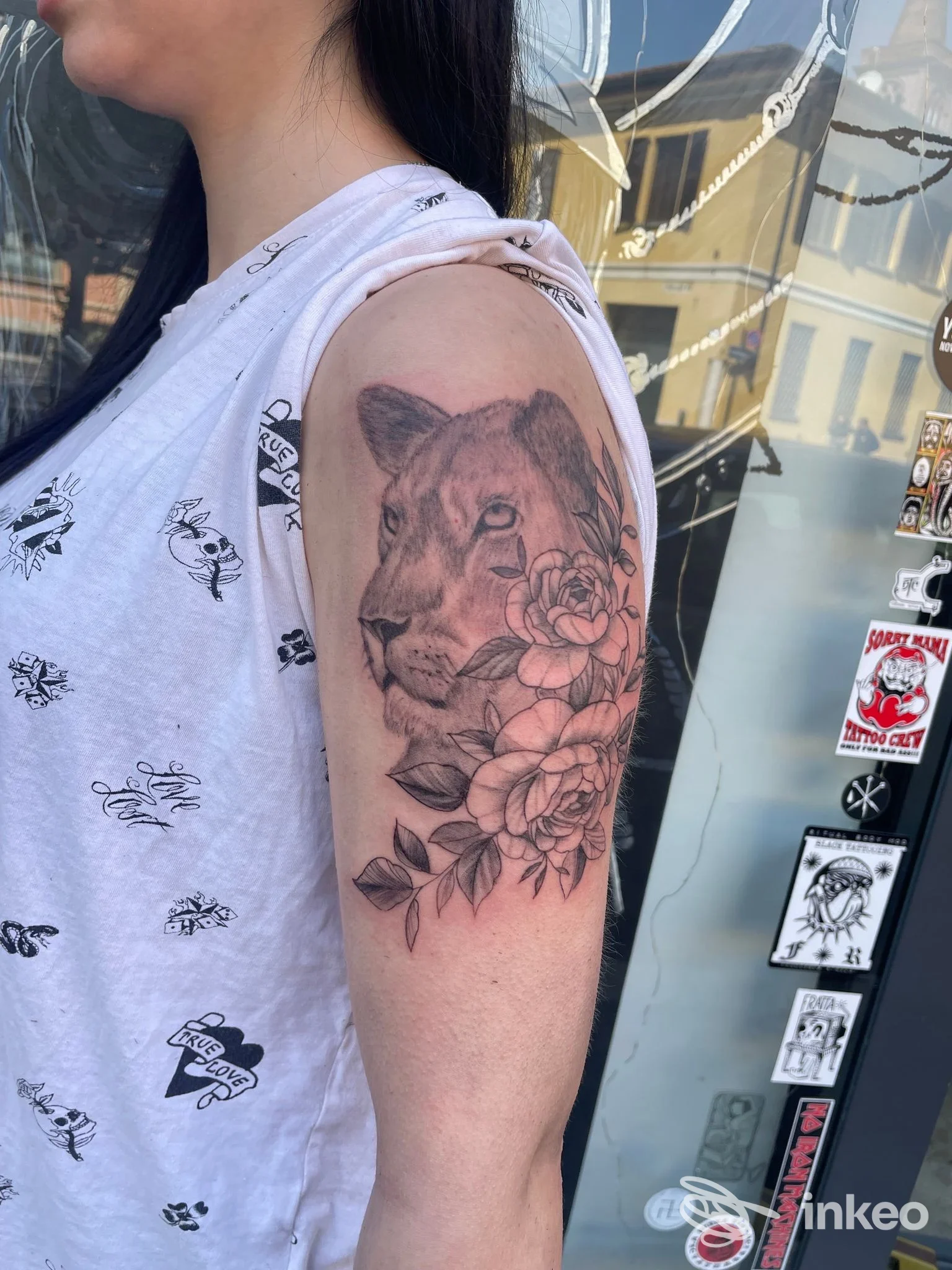 Tattoo realistico di una testa di leone con fiori sul braccio sinistro, visibile chiaramente su pelle reale.