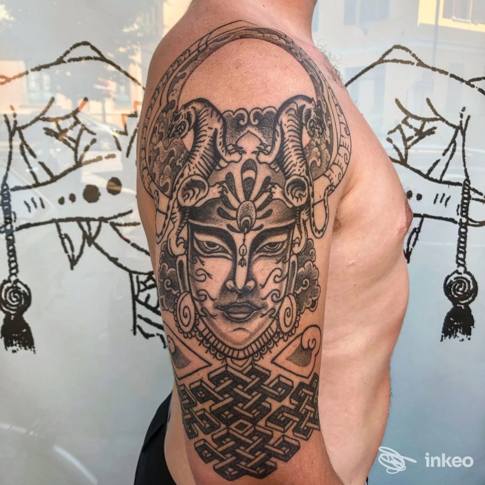 Tattoo visibile sul braccio di una persona: motivo complesso con maschera o volto stilizzato, realizzato direttamente sulla pelle.