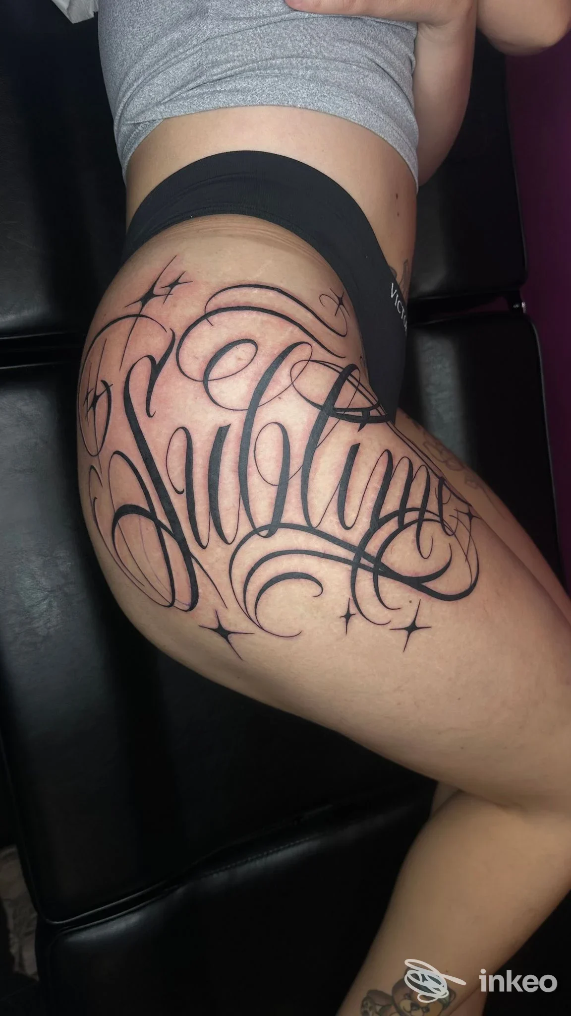Grande tatuaggio calligrafico nero su anca e parte superiore della coscia; immagine fornita da Reborn Tattoo Studio, Torino.