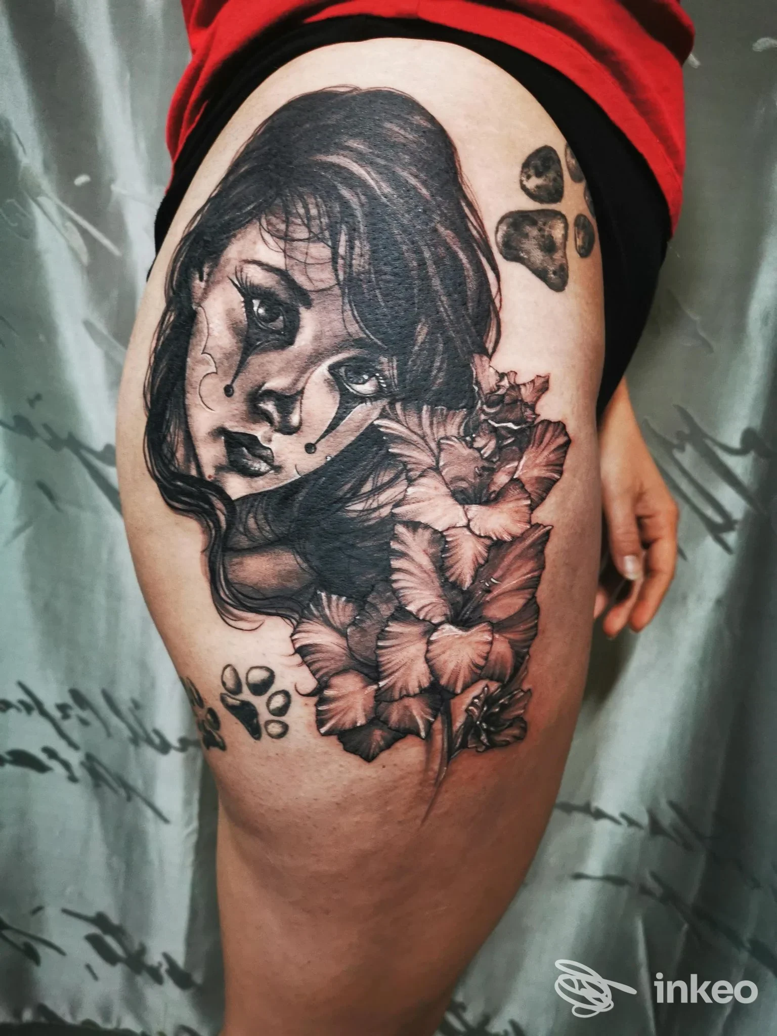 Tatuaggio a Torino dello studio Schizzo Tattoo: grande ritratto femminile in bianco e nero con fiori sulla coscia, visibile pelle e mano laterale.