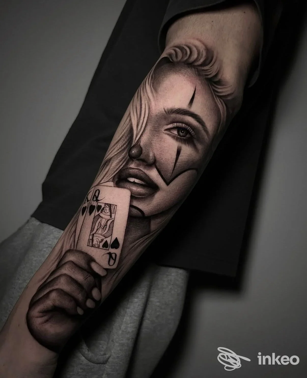 Tatuaggio realistico in bianco e nero sul avambraccio: volto di clown e mano con regina di picche. Stay Gold Tattoo, Borgomanero.