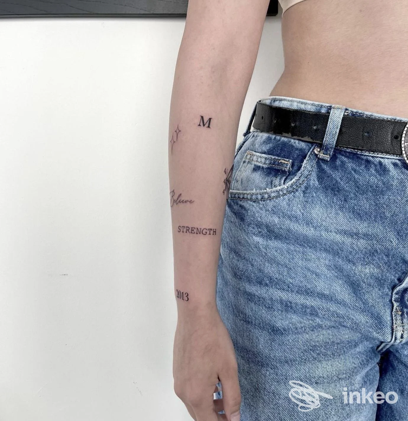 Avambraccio con piccoli tatuaggi minimal neri (lettera M, parola STRENGTH, numeri e simboli), foto per Sons Of Ink - Tattoo & Piercing ad Asti.
