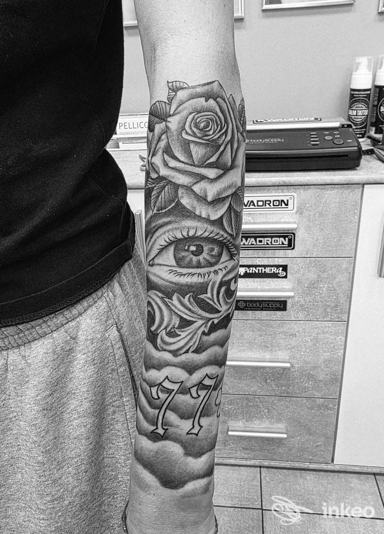Avambraccio tatuato in bianco e nero con rosa, occhio realistico e numeri '77', foto fornita da Tattoolook, Torino.