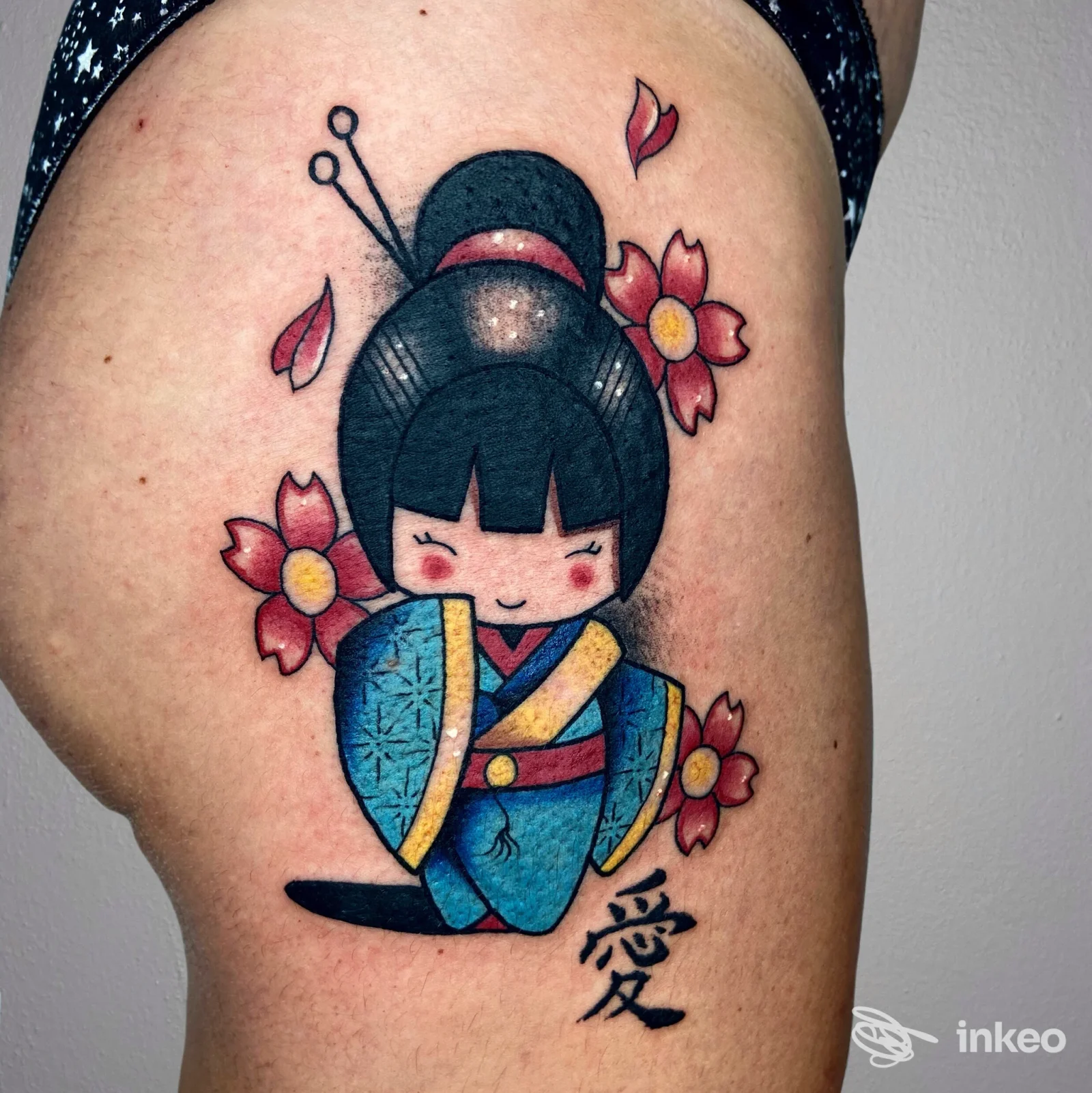 Tatuaggio visibile di una ragazza in kimono blu con fiori rosa, stilizzato, sulla coscia sinistra della persona.