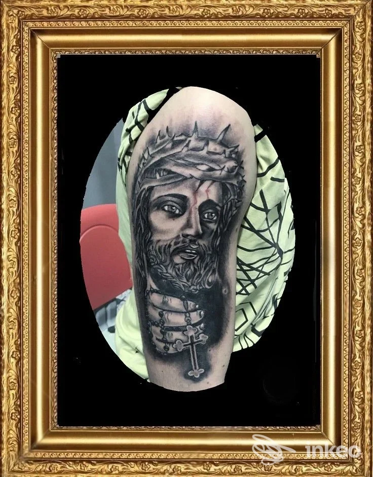Tatuaggio realistico su braccio superiore raffigurante volto con corona di spine e croce — Blues Tattoo, Novara.