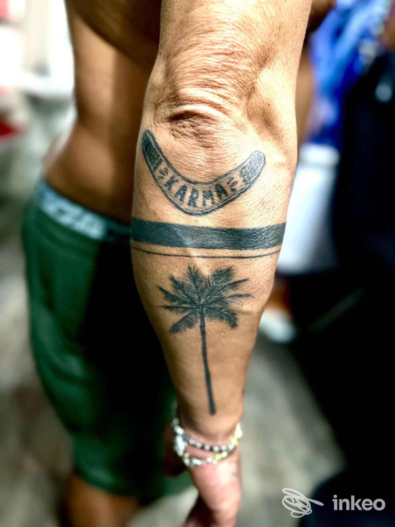 Tattoo all'avambraccio con palma stilizzata e due bande orizzontali; braccia e bracciali visibili, corpo in primo piano.