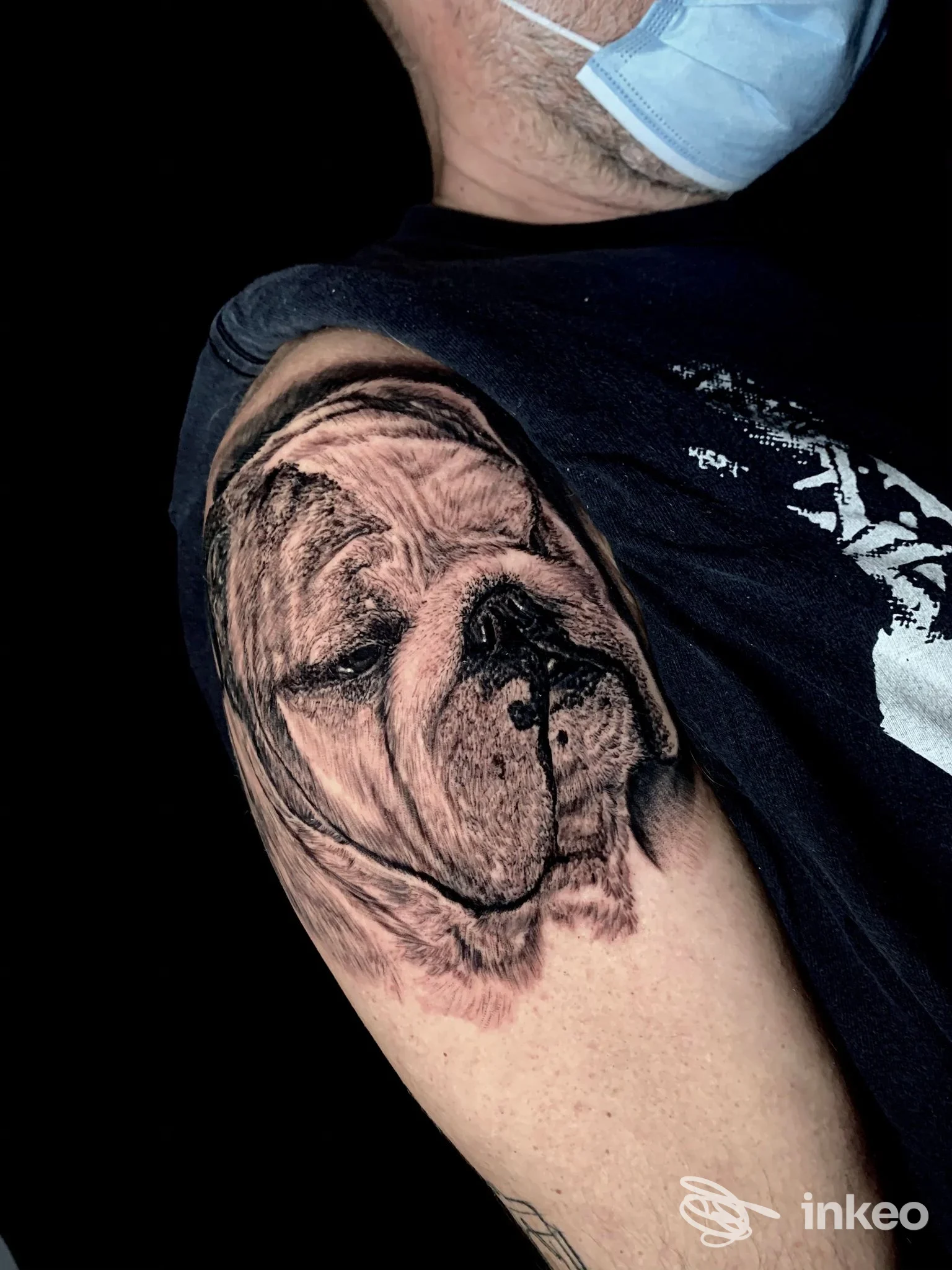 Tatuaggio realistico di cane sul braccio sinistro, tonalità nere e grigie, visibile su pelle umana; senza testo o overlay visibile.