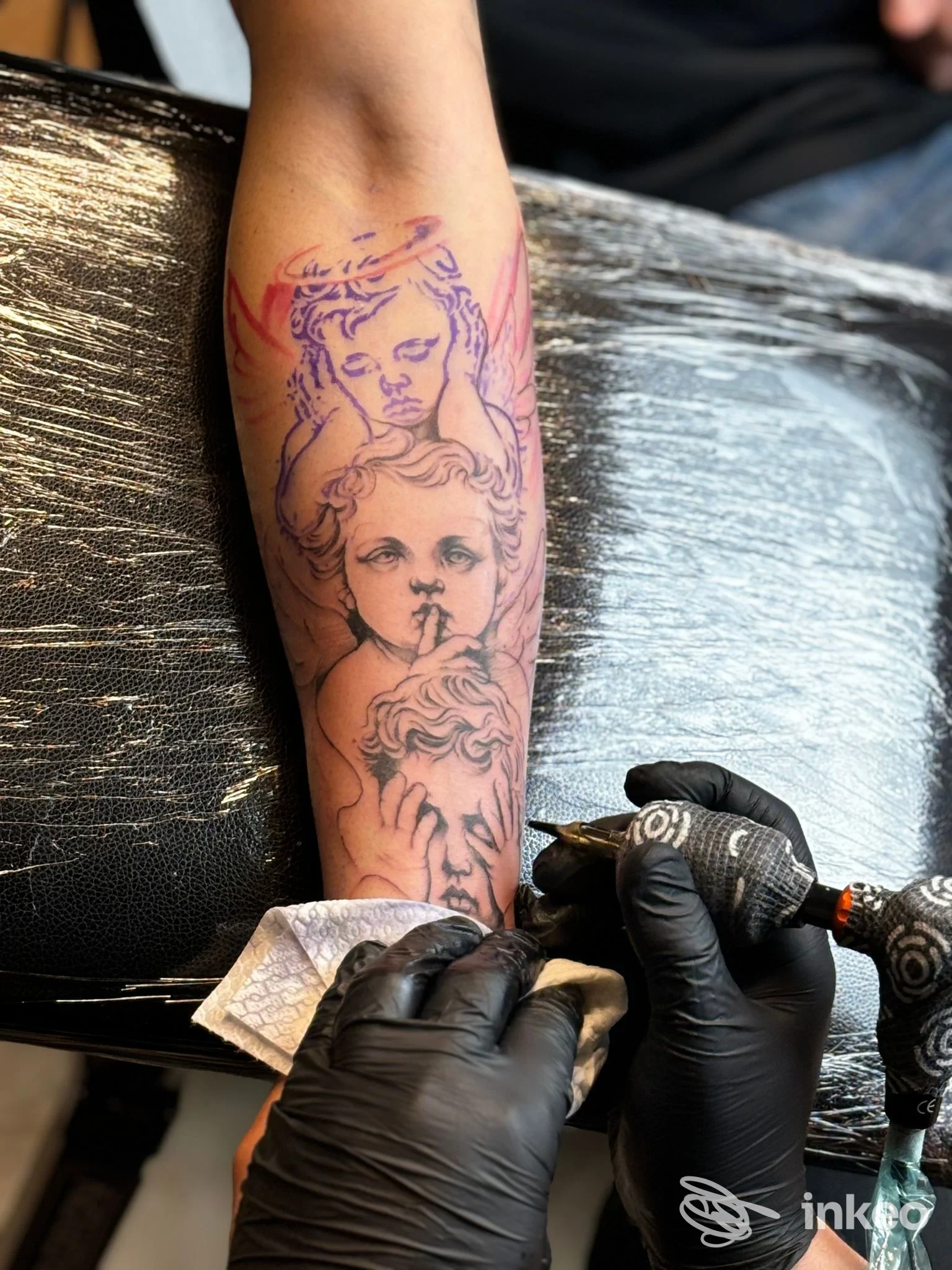 Avambraccio con tatuaggio di due angeli in lavorazione, fotografo mostra l'artista al lavoro; Simor katù tattoo shop, Castellaneta.