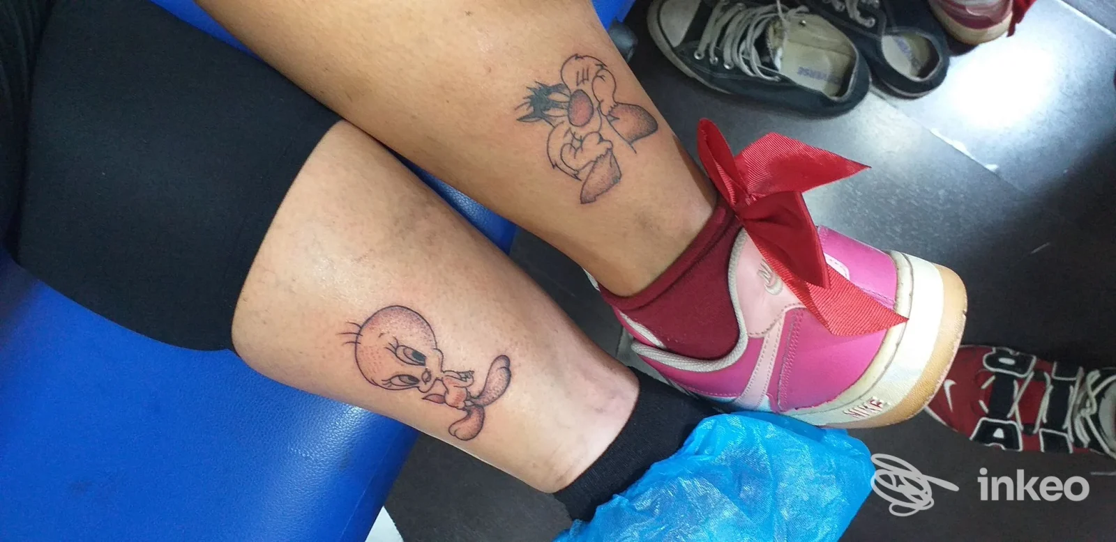 Due tatuaggi in stile cartoon sui polpacci di una persona, vista delle caviglie con scarpe rosa — Skin Project Tattoo Studio, Bari.