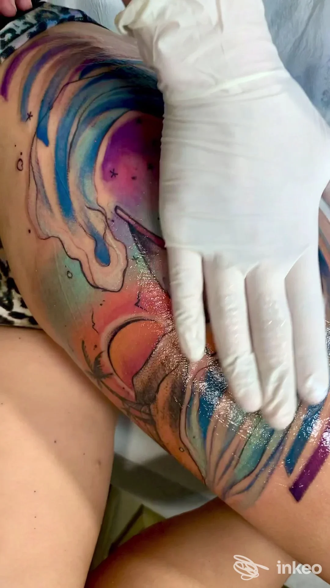 Tatuaggio colorato a onde sulla parte superiore della coscia, artista al lavoro con guanto bianco — Smoun Tattoo, Mola di Bari.