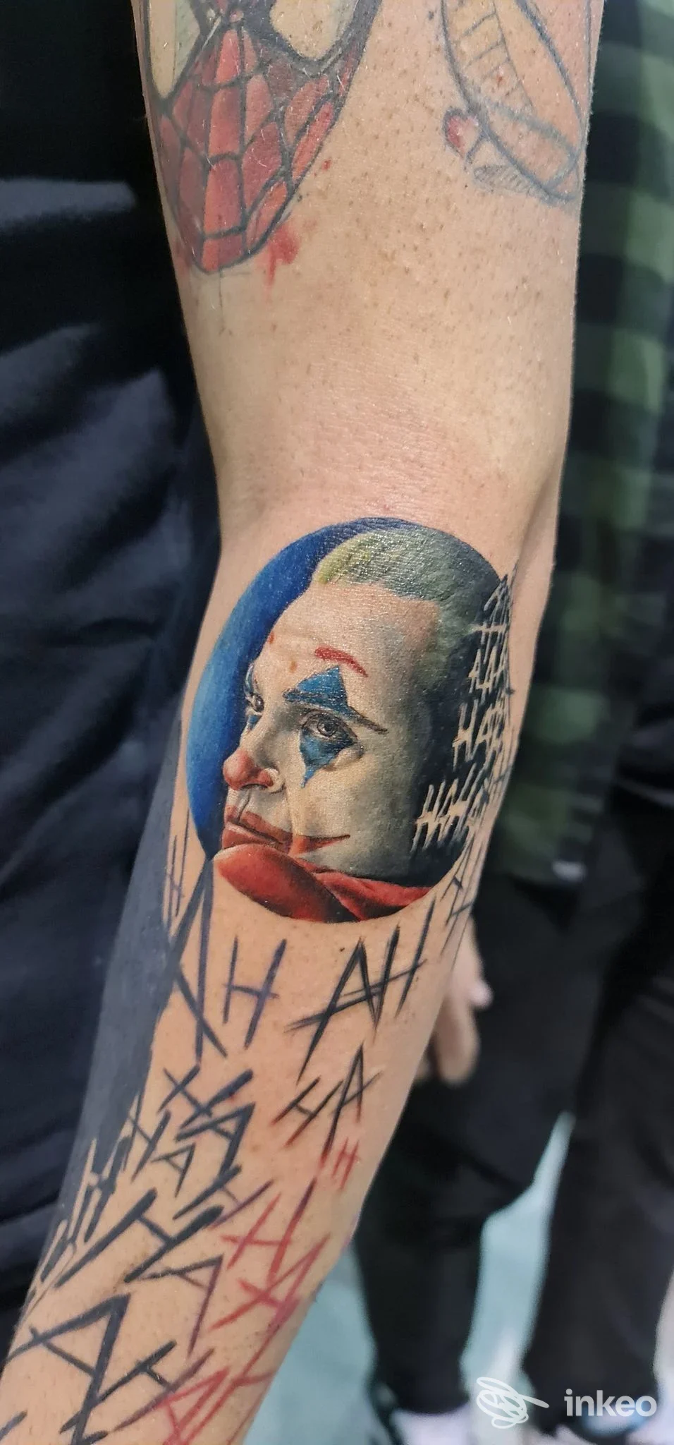 Tatuaggio ritratto in stile Joker su avambraccio, con sfondo blu e segni grafici; Tatuaggificio di Saverio Damiani, Bari.