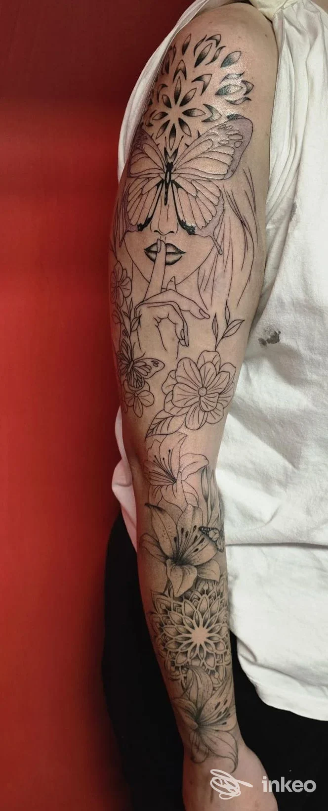 Braccio tatuato a manica completa con donna stilizzata, farfalla e fiori — foto fornita da TATTOO MADE IN CLA È PIERCING, Grottaglie.