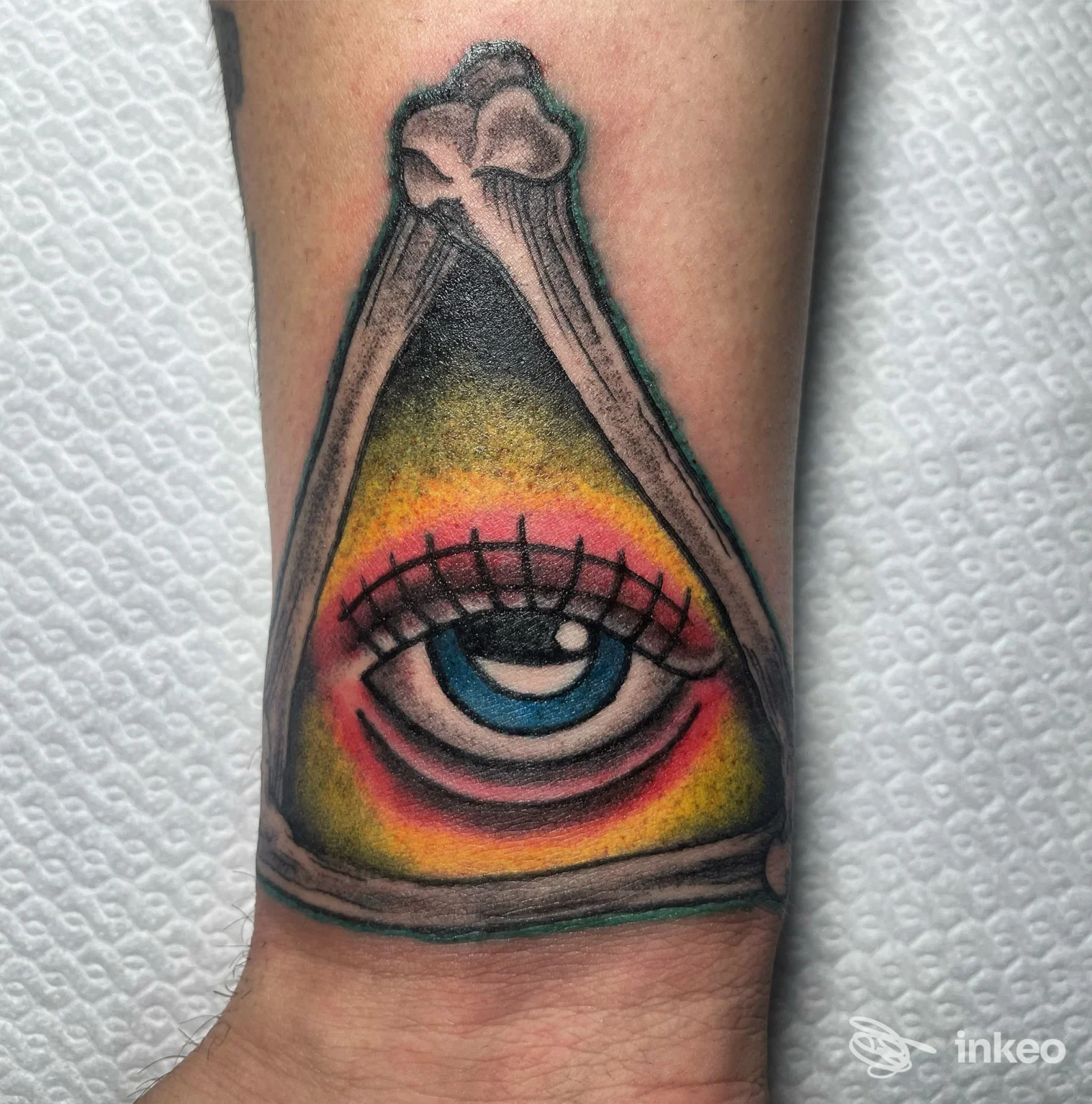 Tatuaggio colorato a forma di triangolo con un occhio al centro sul polso/avampolso, fotografato su pelle. WILD INK TATTOO STUDIO, Martina Franca.