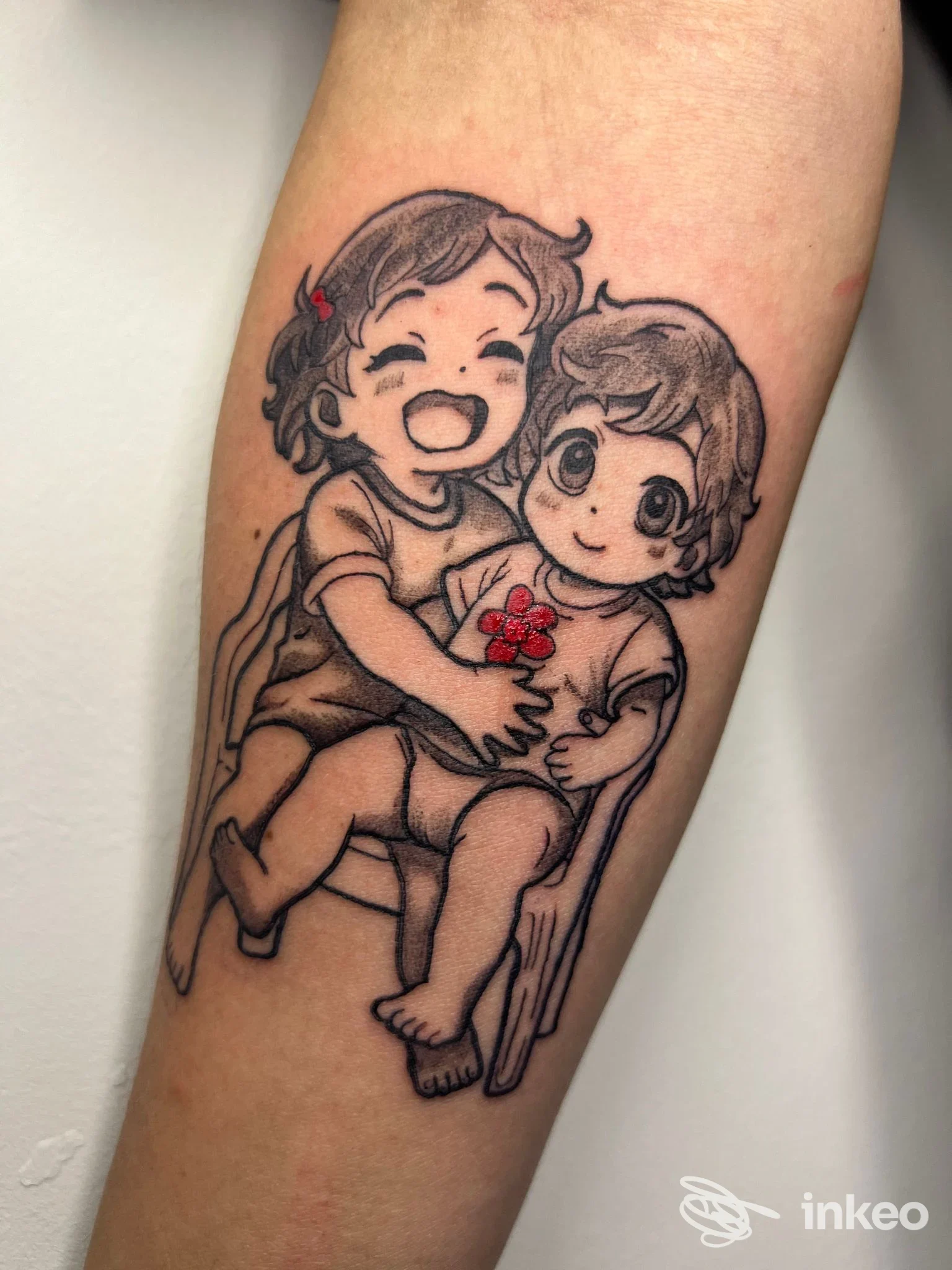 Tatuaggio su avambraccio con due bambini in stile cartoon, dettaglio in nero e piccoli elementi rossi. WILD INK TATTOO STUDIO, Martina Franca.