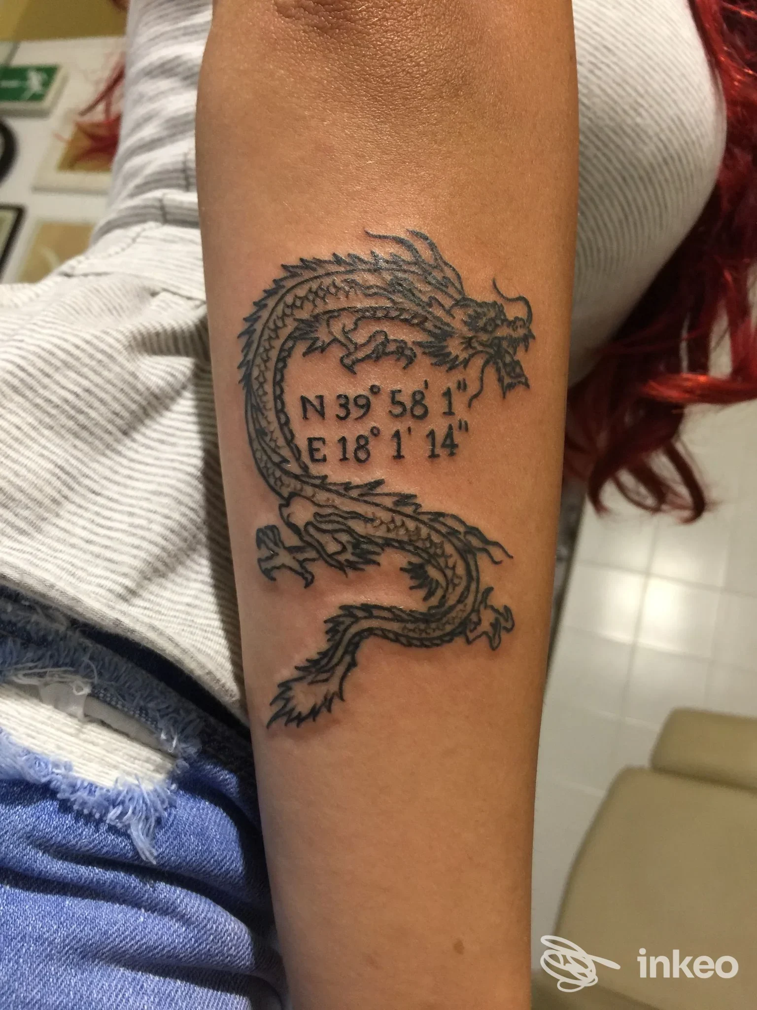Tatuaggio a drago nero con coordinate sull'avambraccio, fotografia fornita da Alex Tattoo, Lecce.
