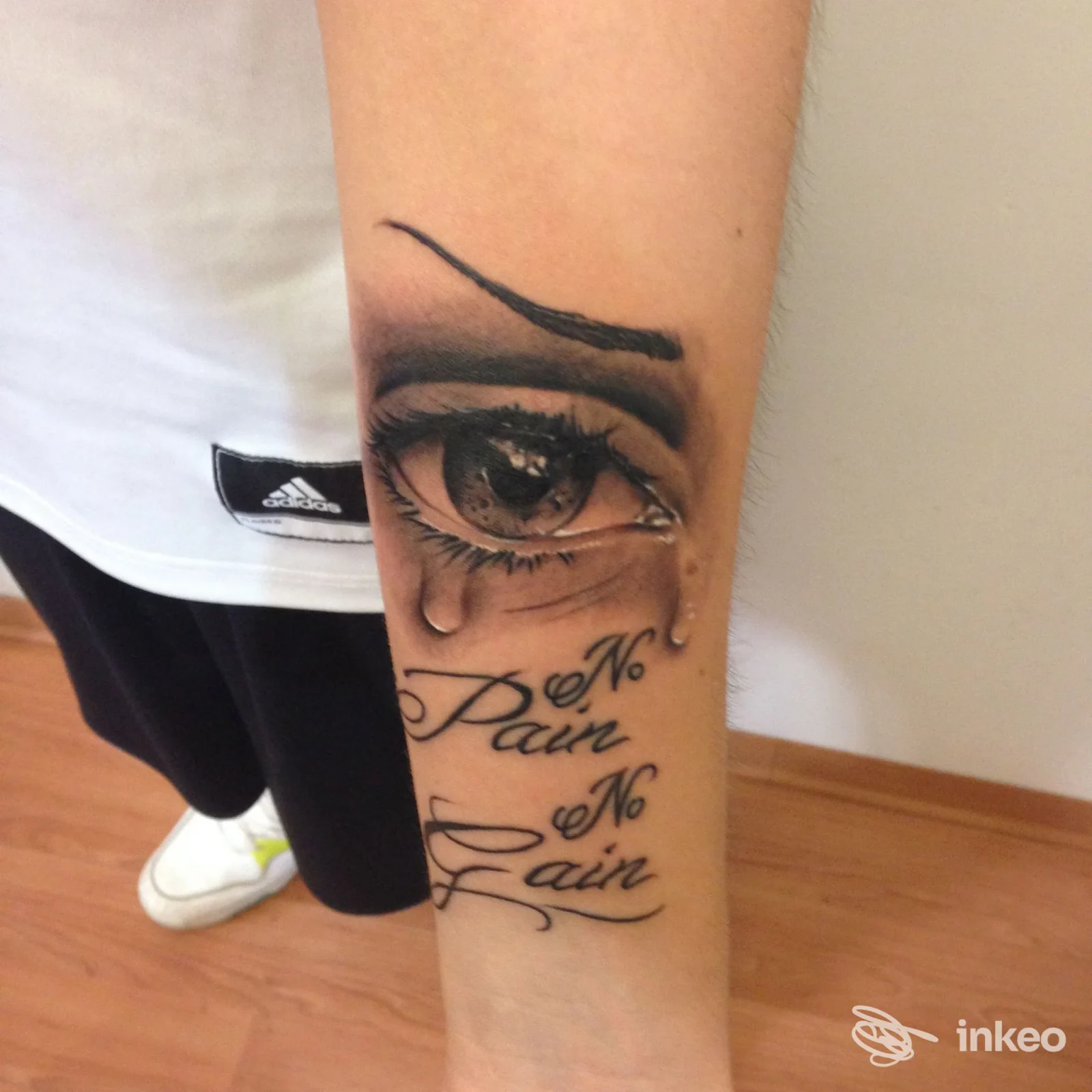 Tatuaggio realistico a occhio con lacrime e scritta 'No Pain No Gain' sull'avambraccio, scatto di Sakura Tattoo Studio Casarano, Casarano.