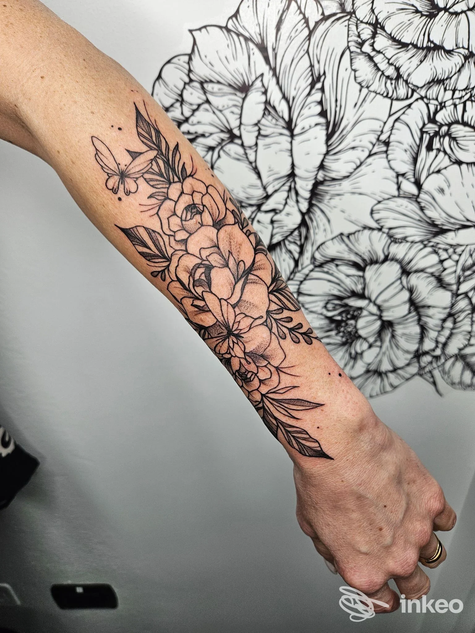 Tattoo floreale su avambraccio realizzato dal studio Mariposa Tattoo, visibile in primo piano, trattamento lineare nero su pelle chiara.