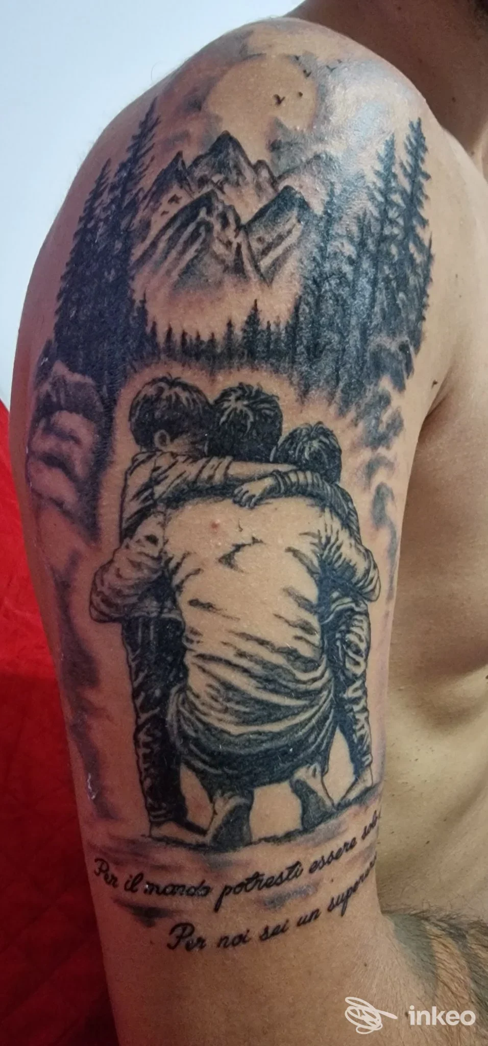 Tattoo realistico su pelle: paesaggio montuoso con alberi e due persone che si abbracciano sulla spalla e parte del braccio; no testo o overlay visibile.