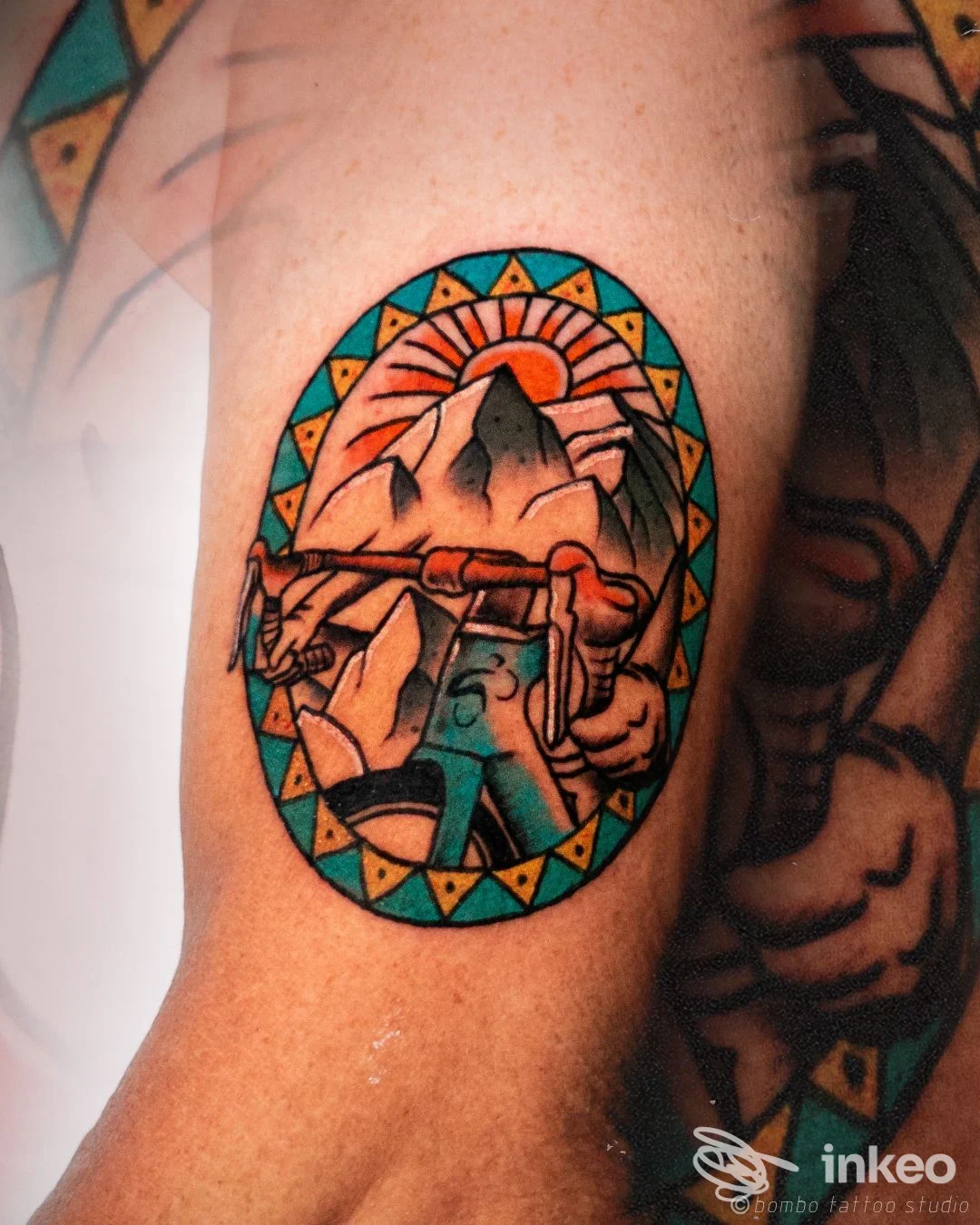 Tatuaggio ovale a colori con paesaggio montano e arrampicatore sul braccio; foto da Bombo Tattoo Studio, Foggia.