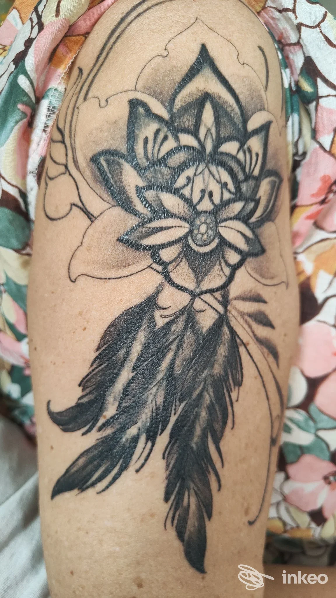Tatuaggio nero a tema floreale con piume sull'esterno del braccio, fotografia per Daimana Tattoo And Piercing Studio, Tricase.