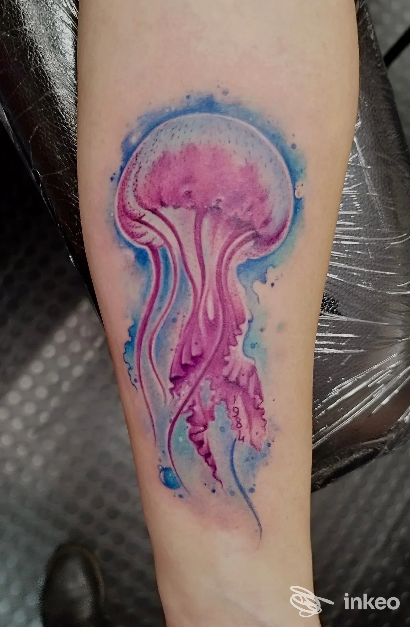 Tatuaggio a medusa in stile acquerello con tonalità rosa e blu sul lato interno dell'avambraccio, fotografato in studio; Evelin Tattoo, Lecce.