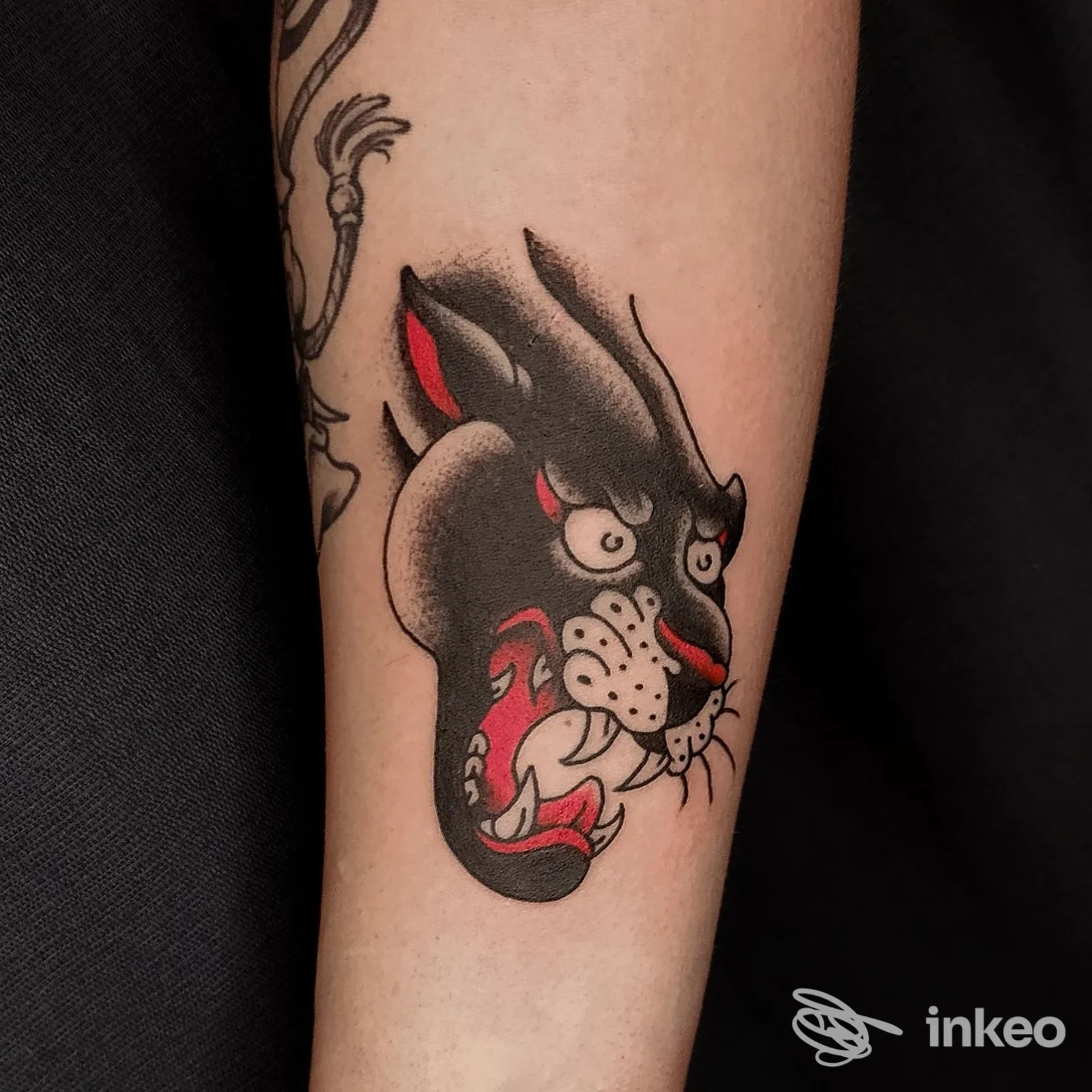 Tatuaggio tradizionale a testa di pantera con neri, rossi e bianchi sull'avambraccio; fotografia nitida eseguita da Freak Ink Tattoo Studio, Bari.