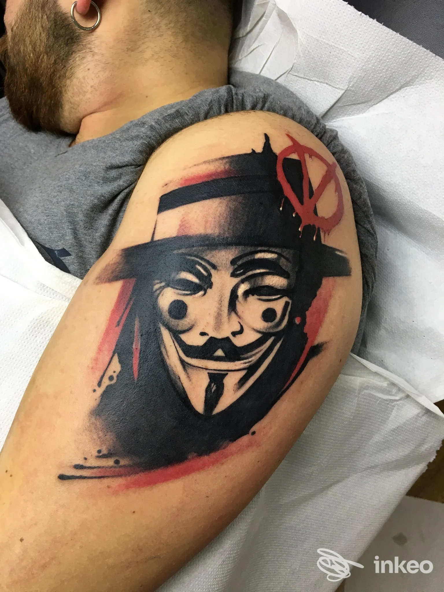 Tatuaggio grande sul deltoide con maschera stilizzata in nero e rosso, Glam Tattoo di Enea Polimeno a Melpignano.