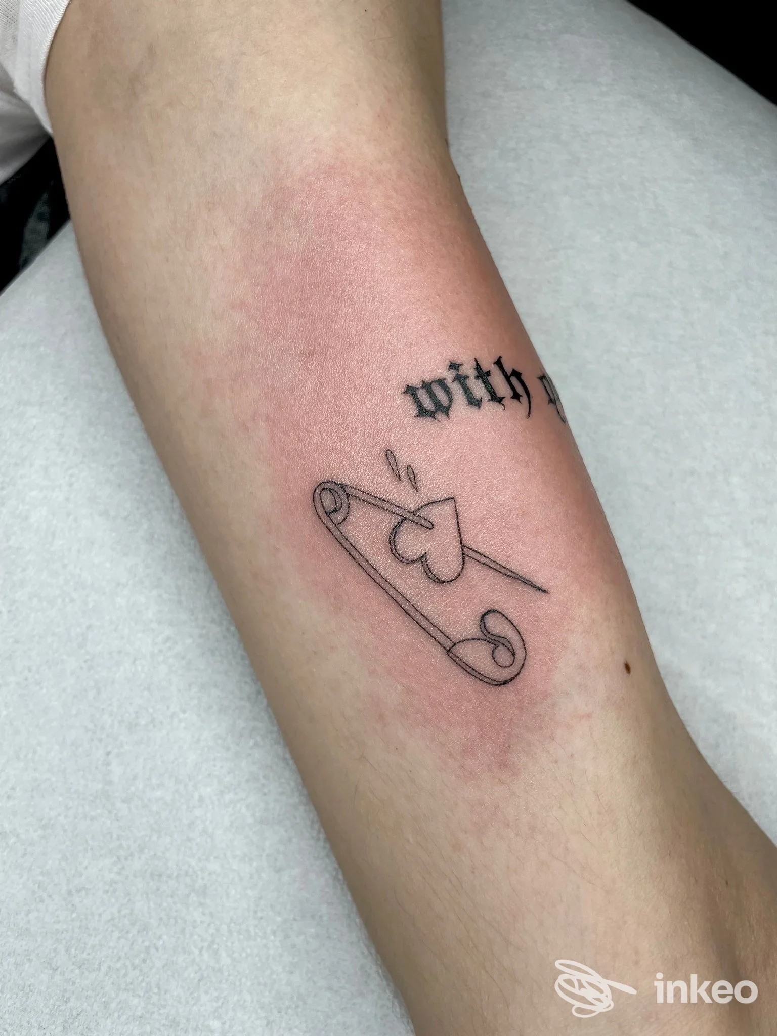 Tatuaggio a linee di una spilla da balia con cuore sull'avambraccio, eseguito presso Goldeneedles tattoo shop, Brindisi.