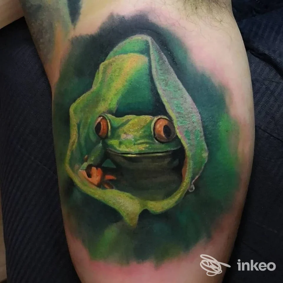 Tatuaggio realistico di una rana verde incorniciata da una foglia, realizzato sulla pelle, colori vividi e sfumature morbide.