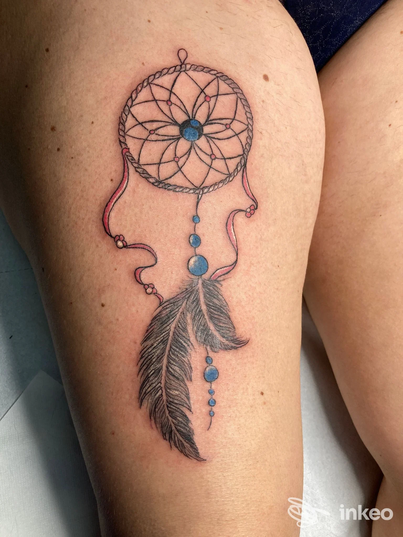 Tatuaggio acchiappasogni con perle blu, nastri rosa e piuma sulla coscia, IDA TATTOO STUDIO, Foggia.