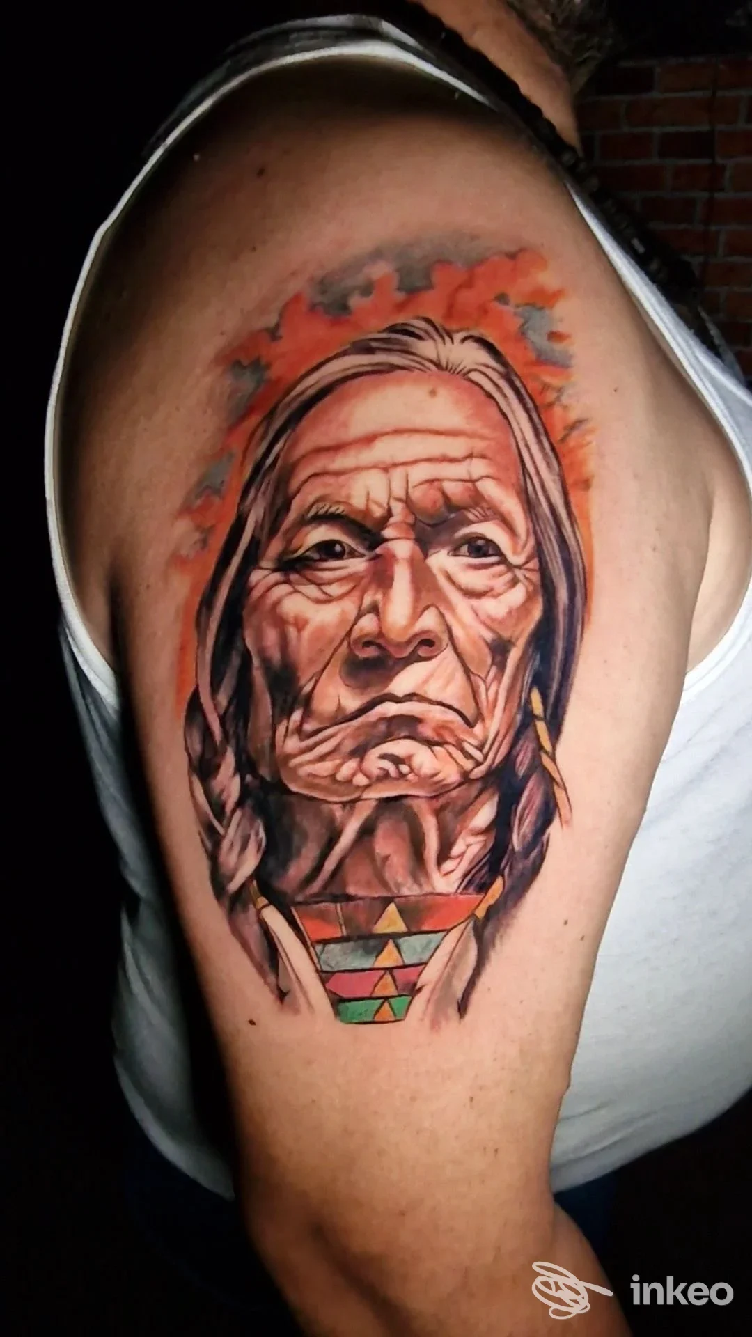 Tatuaggio realistico a colori sul braccio superiore raffigurante il volto di un anziano; immagine fornita da INKLAM TATTOO STUDIO, Canosa di Puglia.