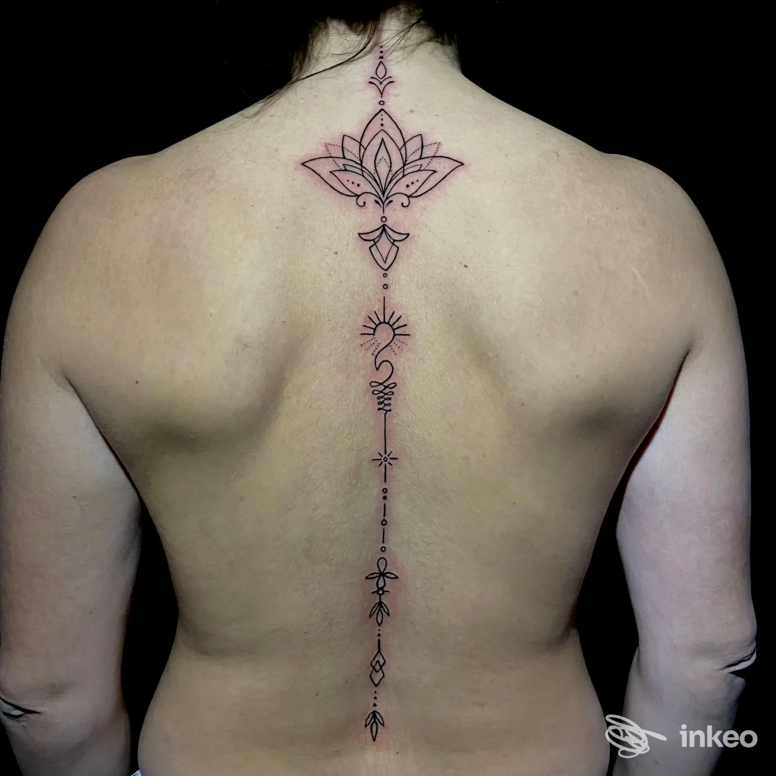 Tatuaggio ornamentale a linea centrale sulla schiena, motivo a loto in alto e elementi geometrici lungo la colonna vertebrale.