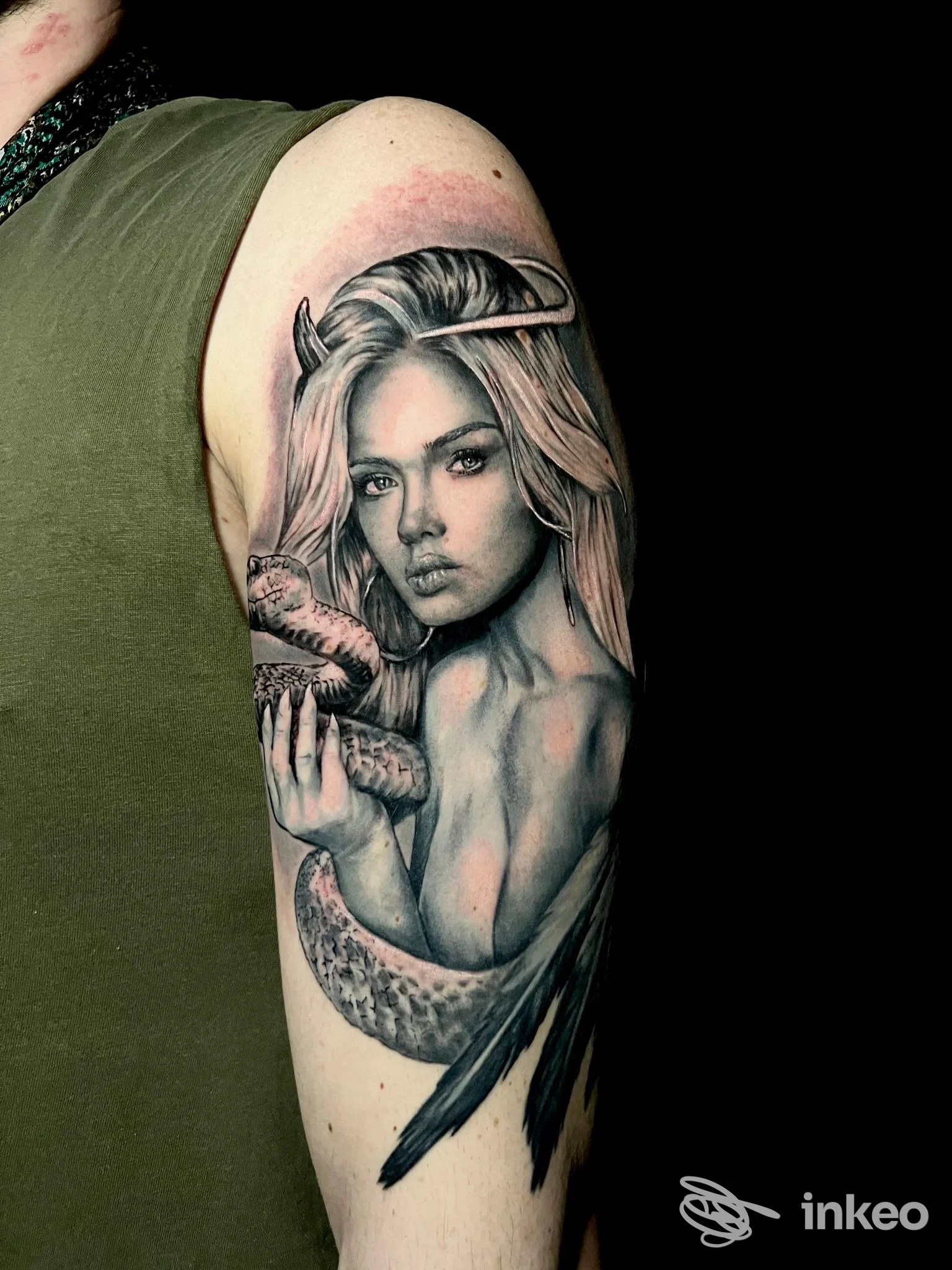 Tattoo realistico su braccio raffigurante una figura femminile, con serpente avvolto attorno al braccio; sfondo nero.