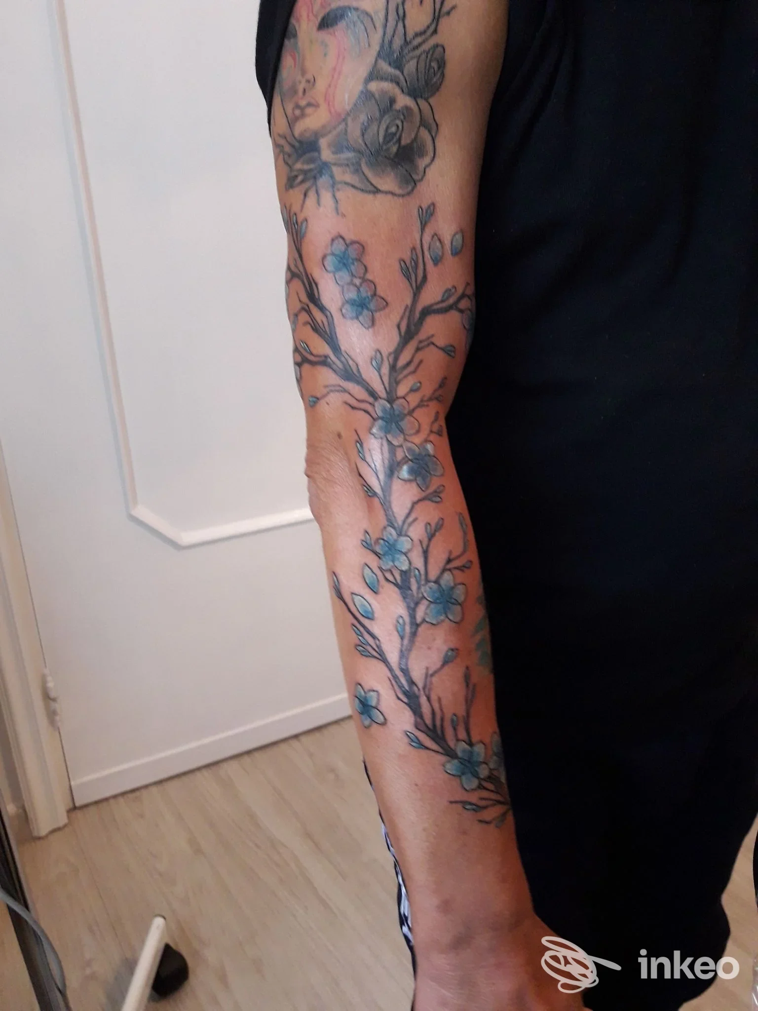 Avambraccio tatuato con ramo fiorito e fiori blu, fotografia inviata da La Tatueria - Santeramo In Colle, vista intera dell'avambraccio.