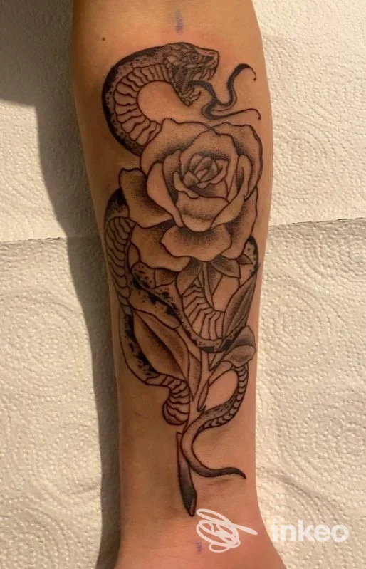 Tatuaggio a inchiostro nero di serpente avvolto attorno a una rosa sull'avambraccio. M20INK TATTOO & PIERCING, Ceglie Messapica.