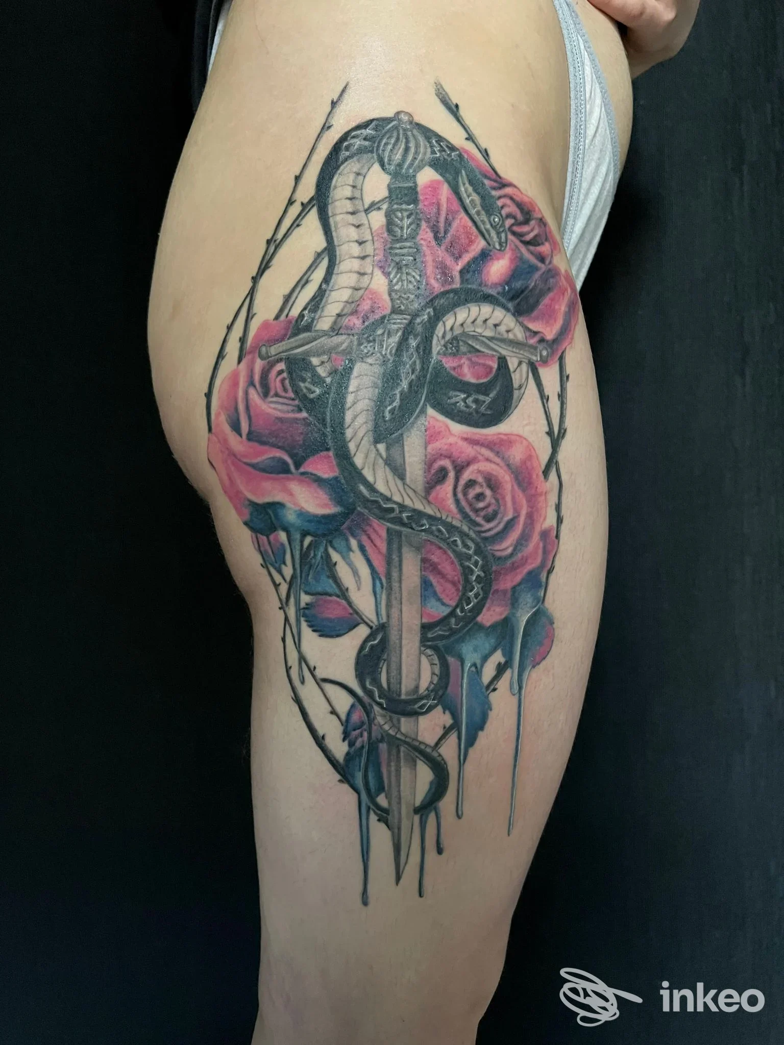 Tatuaggio realistico di serpente avvolto attorno a una spada con rose e filo spinato sulla coscia, eseguito da MANCHADEARTE TATTOO STUDIO a Muro Leccese.
