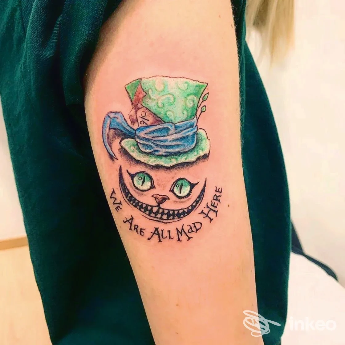 Tatuaggio colorato sul braccio superiore raffigurante il Cappellaio/Gatto sorridente. Nanuk Tattoo Studio, Bari.