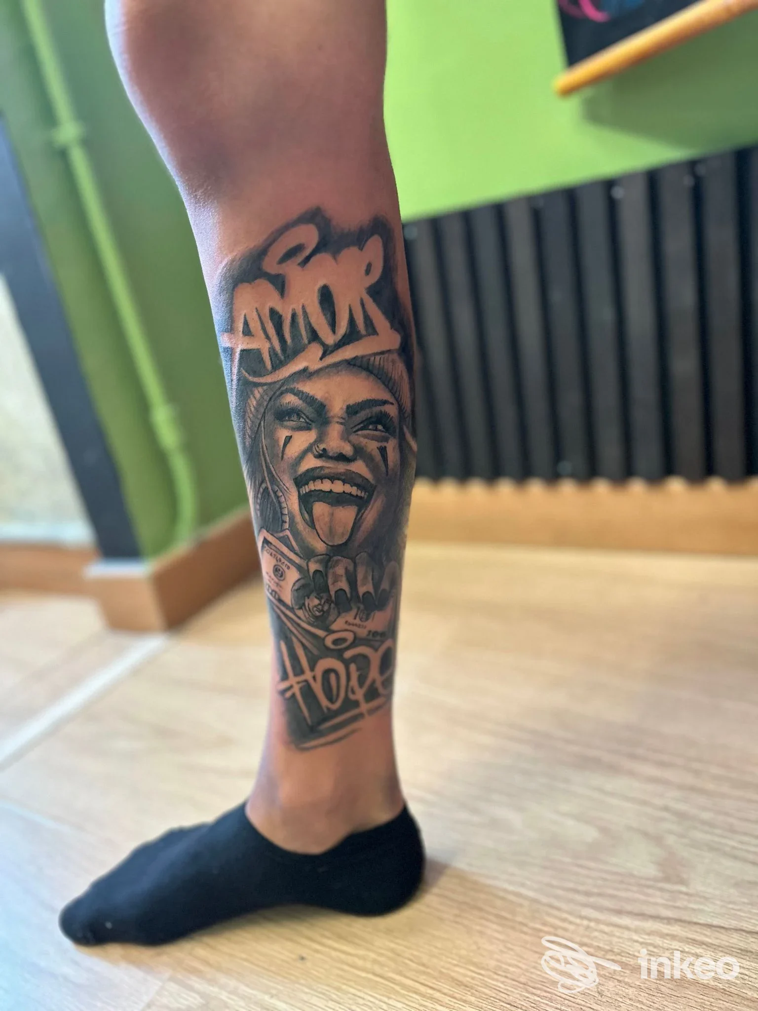 Tatuaggio black & grey su polpaccio con volto stilizzato e scritta 'AMOR' — Nanuk Tattoo Studio, Bari.