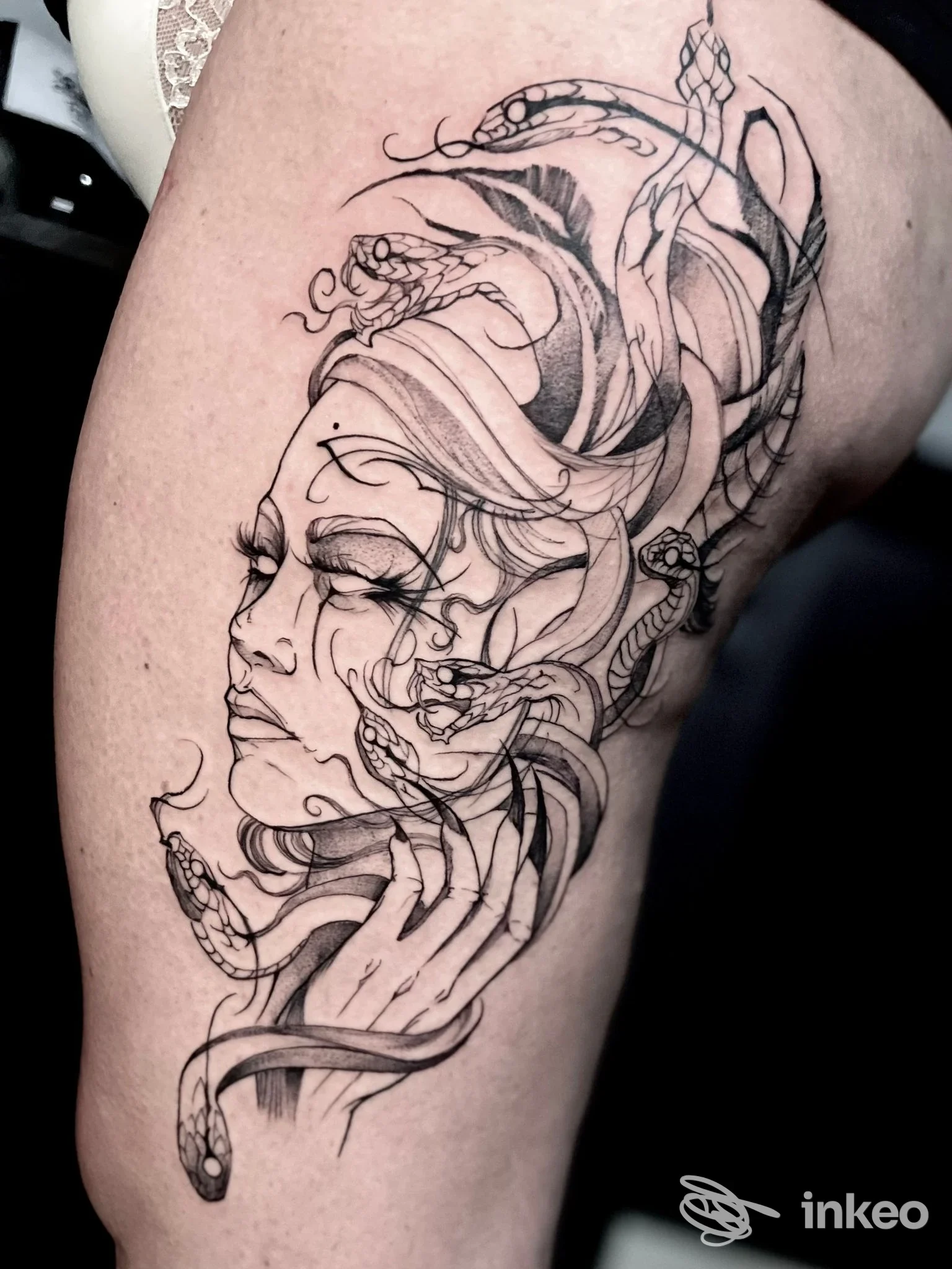 Tatuaggio in bianco e nero su coscia con volto stilizzato e serpenti — OFFICINA LUX TATTOO LAB, Foggia.