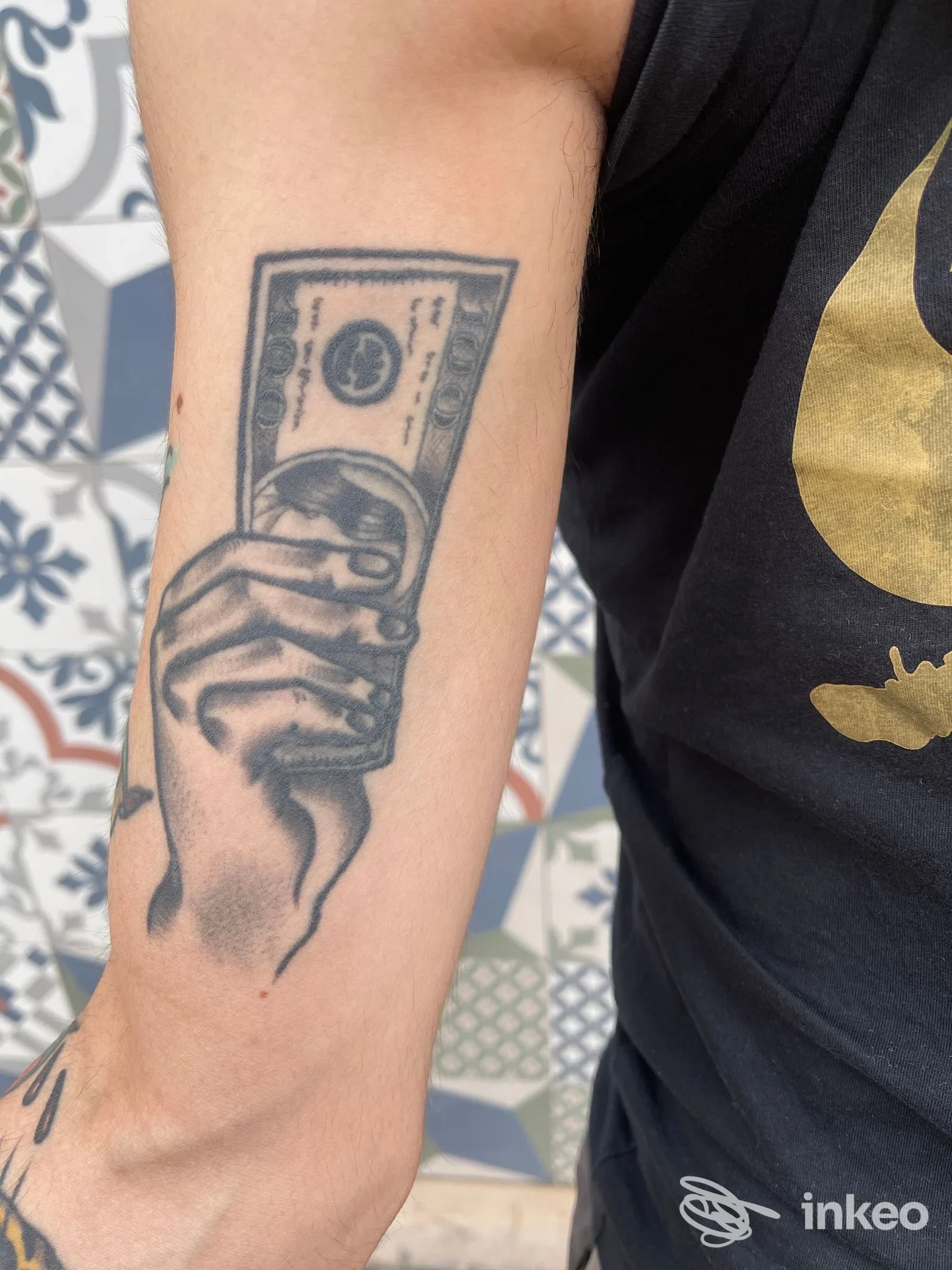 Tatuaggio su avambraccio raffigurante una mano che tiene una banconota — Old times tattoo studio, Spinazzola.