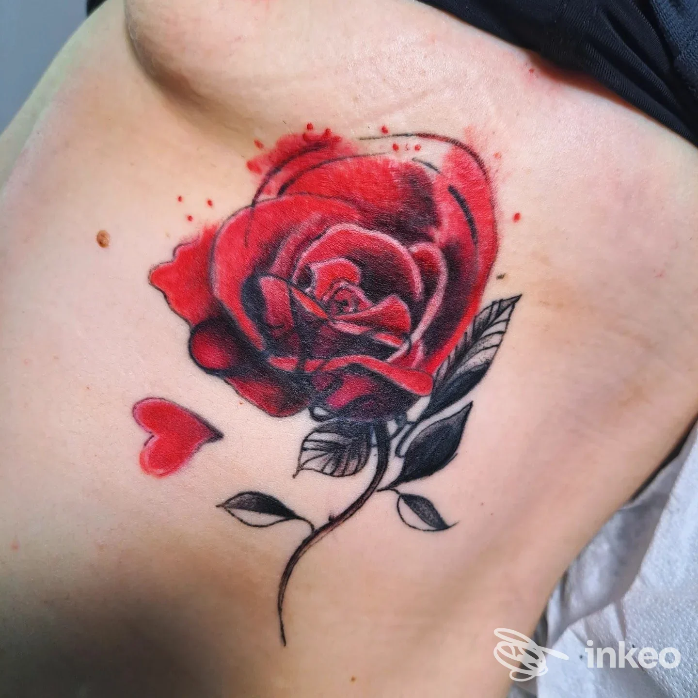 Tatuaggio a colori di una rosa rossa con stelo e foglie nere sul fianco, Michelle Tattoo, Leporano.