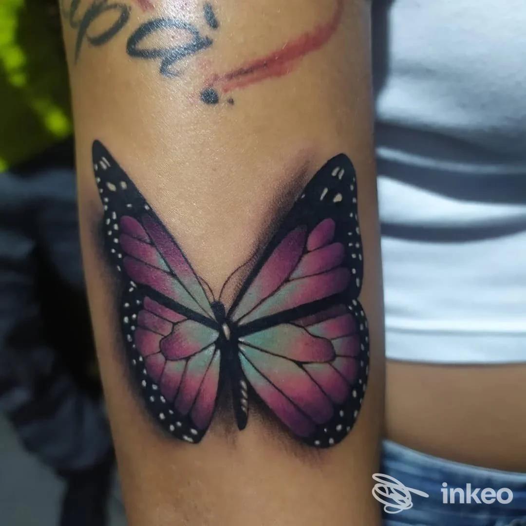 Tattoo di una farfalla colorata sulle braccia, con sfumature rosa, viola e verde e contorni neri. eseguito dallo studio Ale Buzzi a Verano Brianza.