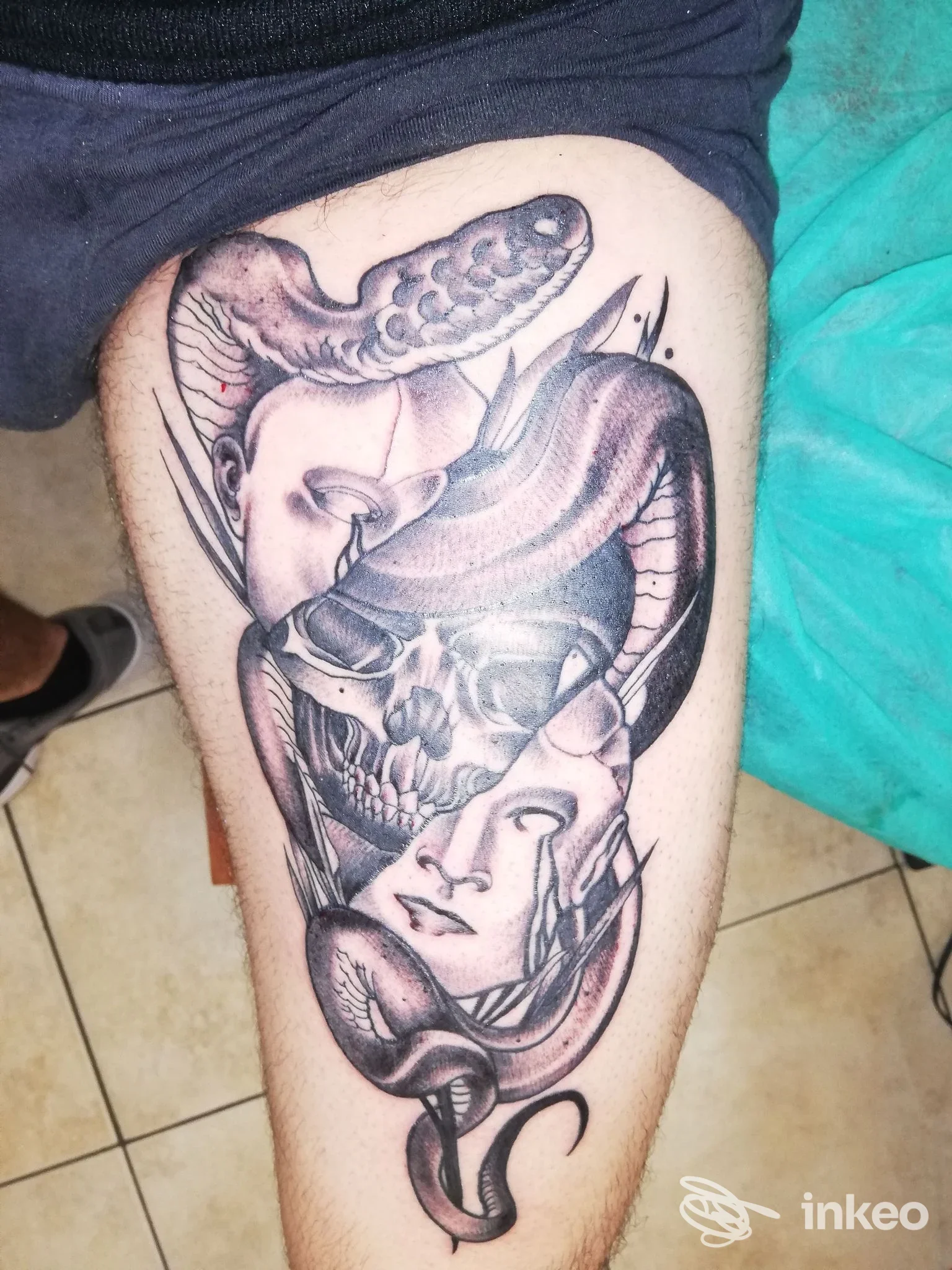 Tatuaggio black & grey su coscia con volti stilizzati, teschio e serpente, foto condivisa da DEATH KISS TATTOO, Foggia.