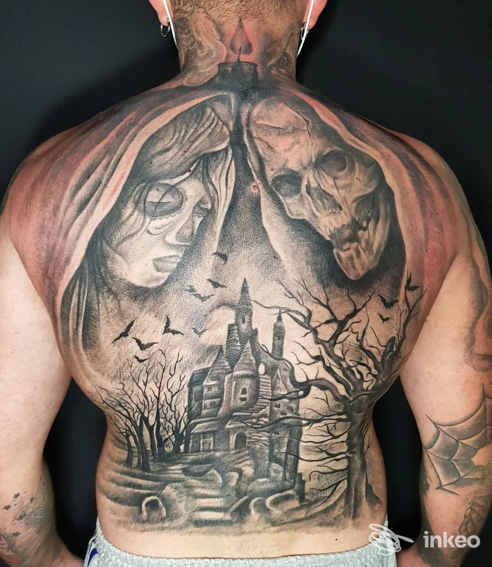 Ampio tatuaggio sulla schiena raffigurante casa stregata, alberi, pipistrelli e due volti; immagine fornita da Black Cat Tattoo by Cinzia Santoro, San Vito dei Normanni.
