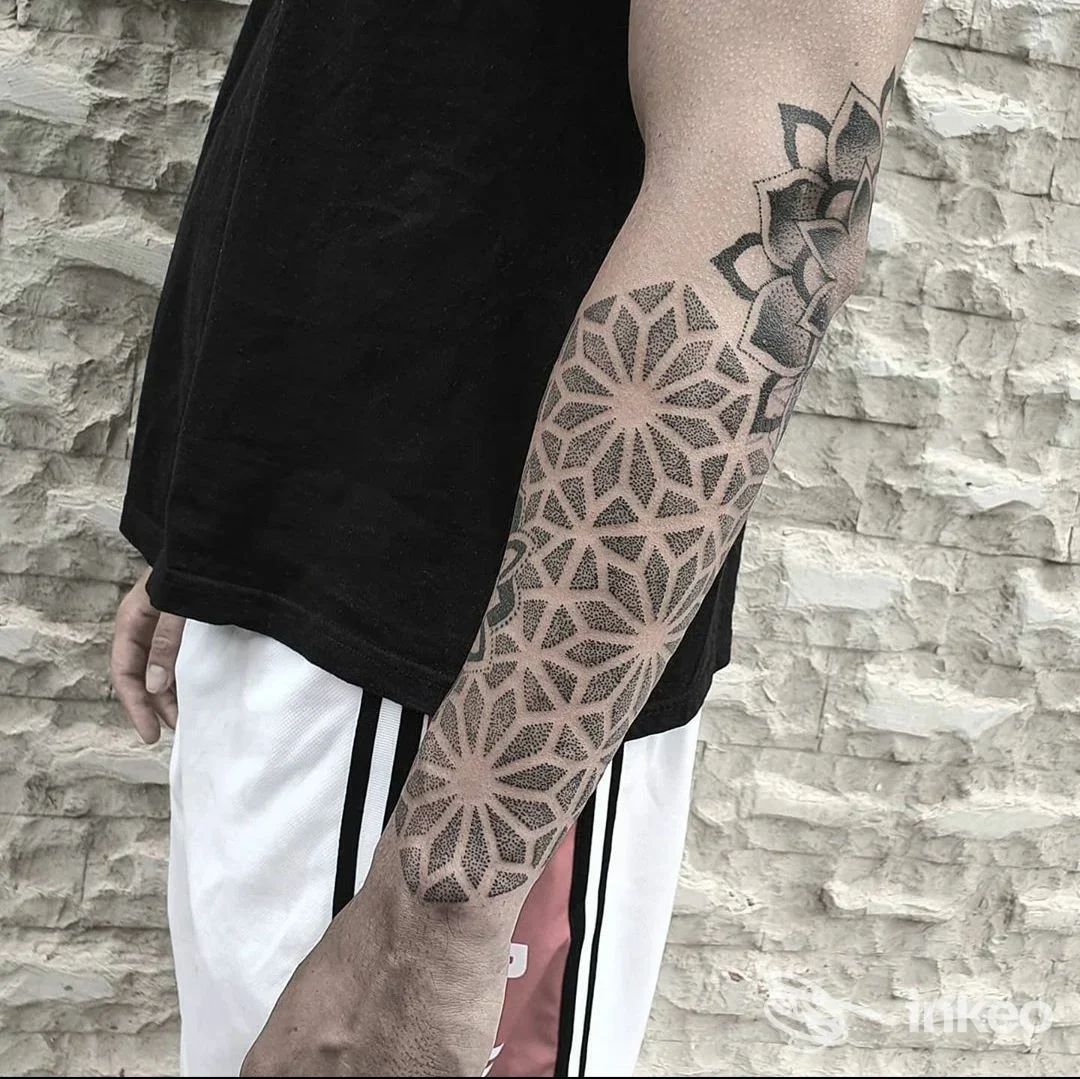 Dettaglio di manica geometrica dotwork sull'avambraccio, sfondo muro di pietra; foto di Endless River Tattoo a Foggia.