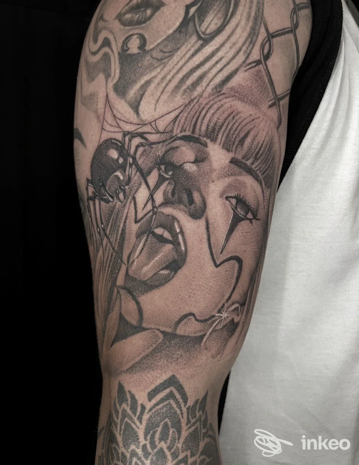 Primo piano di un tatuaggio in bianco e nero a mezzo manica sul braccio con volto stilizzato e dettagli decorativi; Free Art Tattoo, Castellaneta.