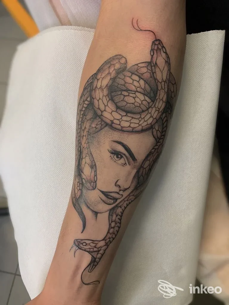 Tattoo sull’avambraccio raffigurante una testa di donna avvolta in una grande serpente, realizzata in toni neri e grigi.