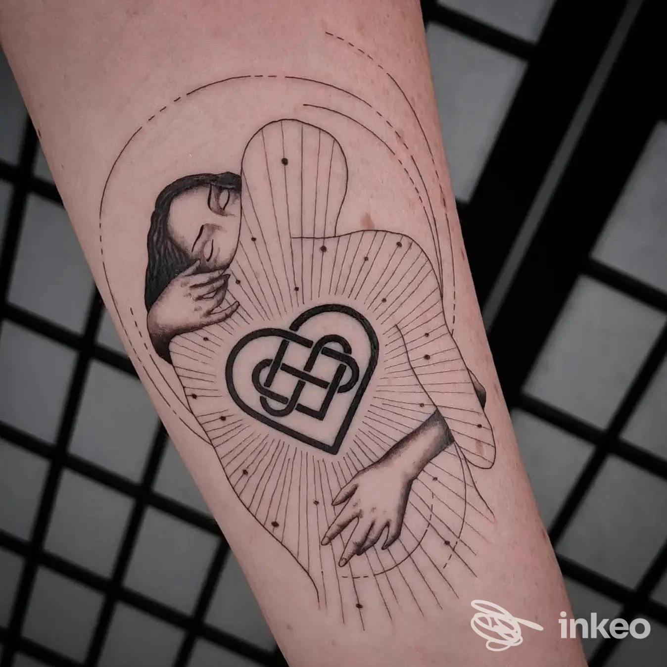 Tattoo su avambraccio sinistro raffigurante una mano e una figura femminile all'interno di un cuore intrecciato, circondata da linee radianti.