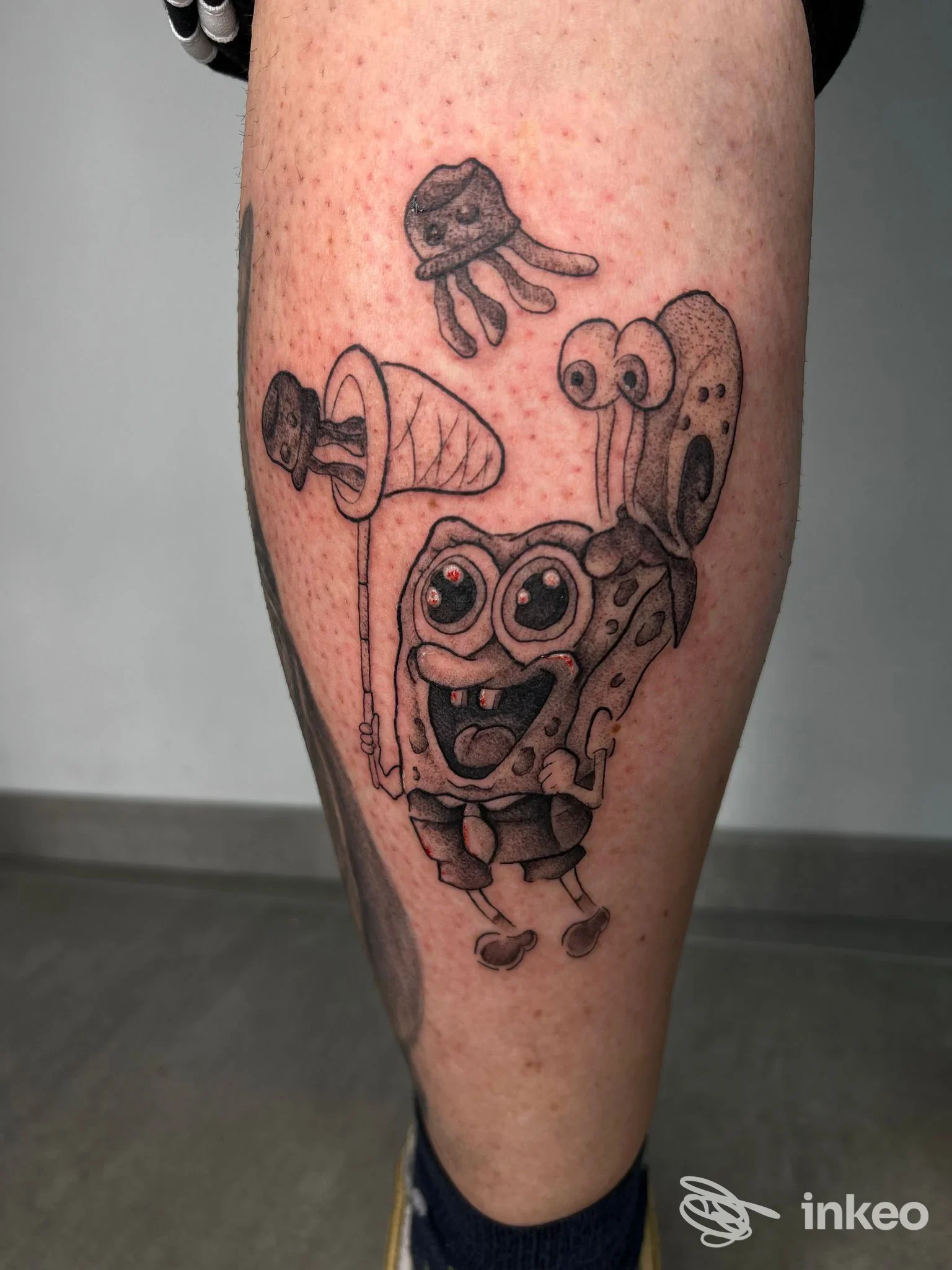 Tatuaggio in bianco e nero su polpaccio raffigurante SpongeBob che cattura meduse, MAAD Tattoo Shop Matino.